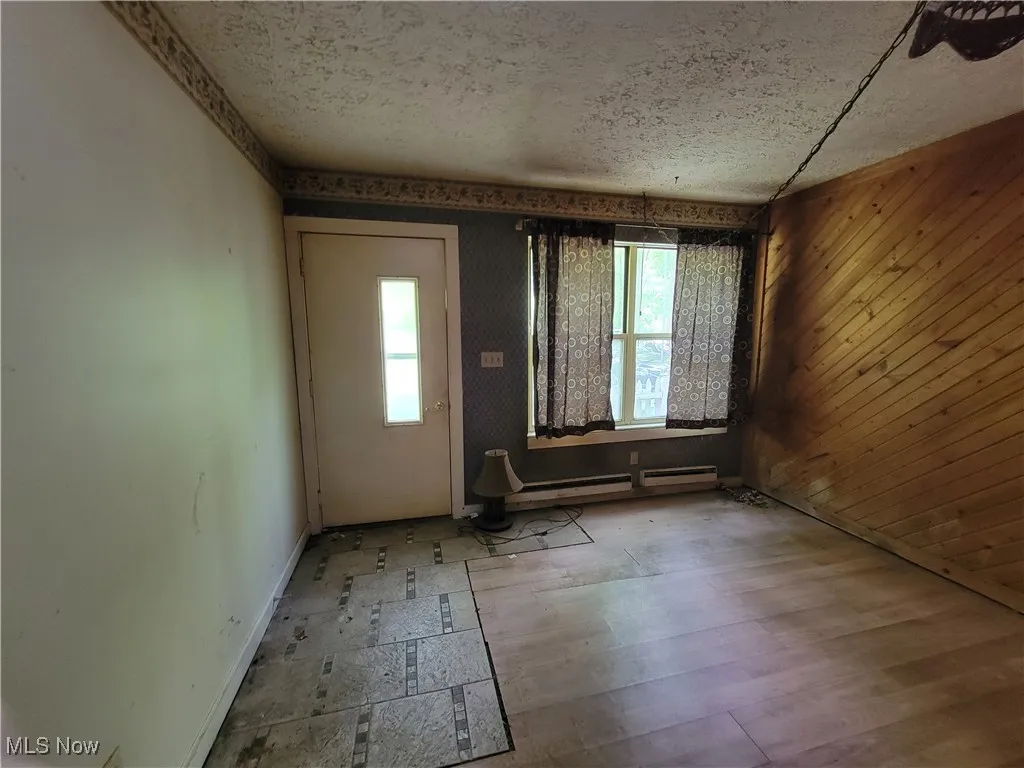 Entryway with a textured ceiling, baseboard heating, and wooden walls