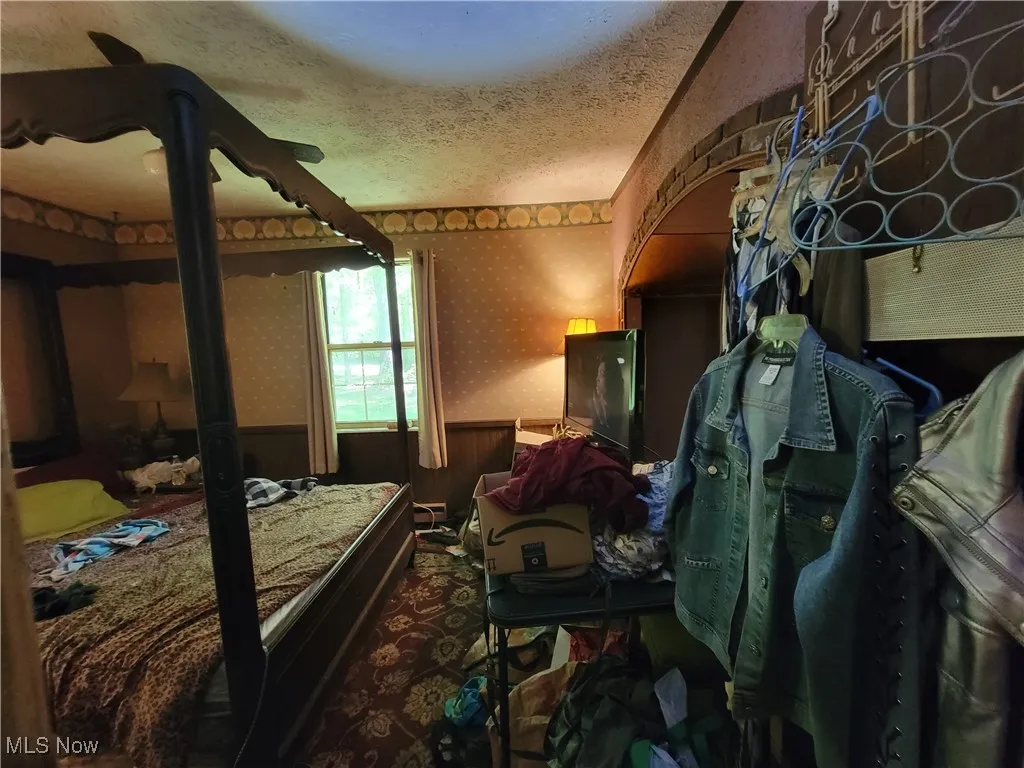 Bedroom with wallpapered walls, a wainscoted wall, a textured ceiling, and carpet