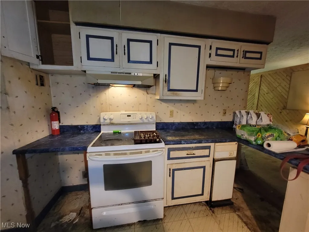 Kitchen featuring electric range, under cabinet range hood, wallpapered walls, and dark countertops