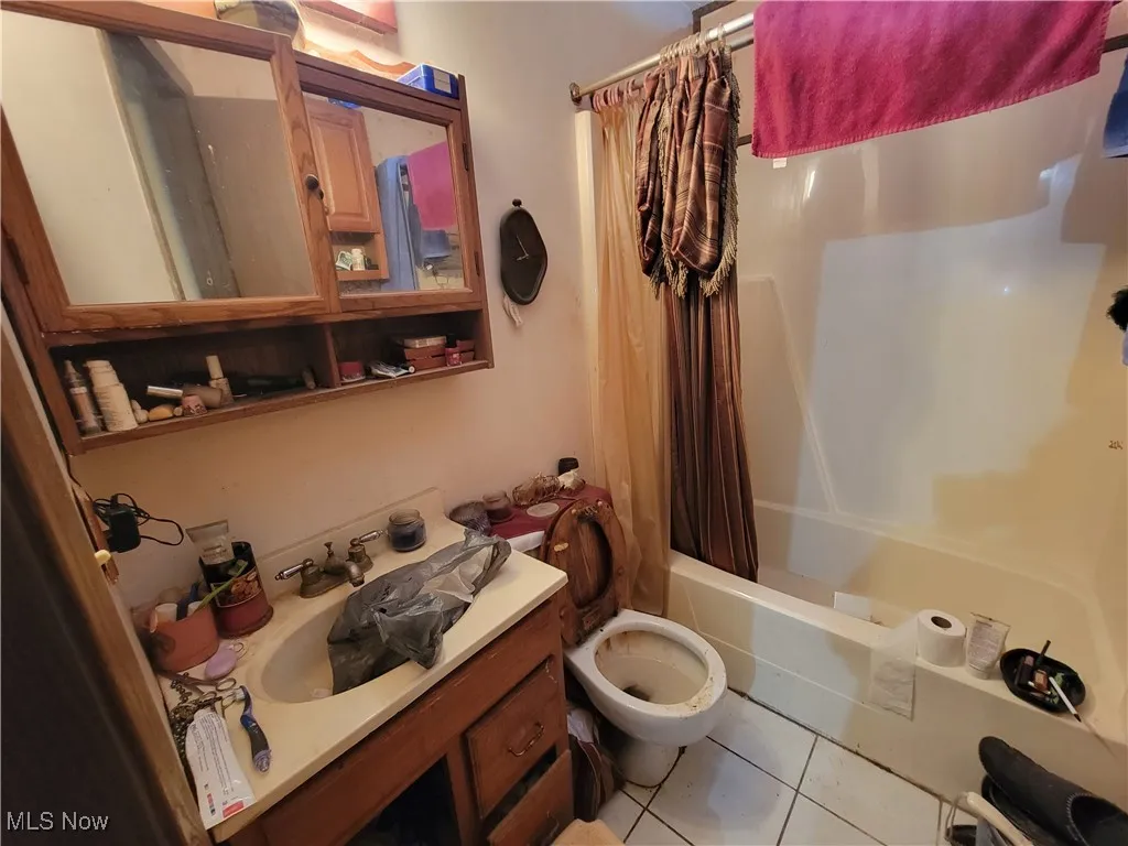 Bathroom with tile patterned floors, shower / bath combo with shower curtain, and vanity