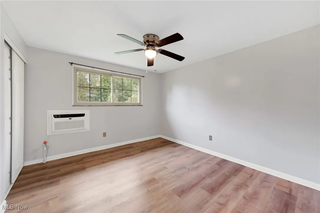 Unfurnished bedroom with a closet, wood finished floors, a wall mounted AC, and ceiling fan
