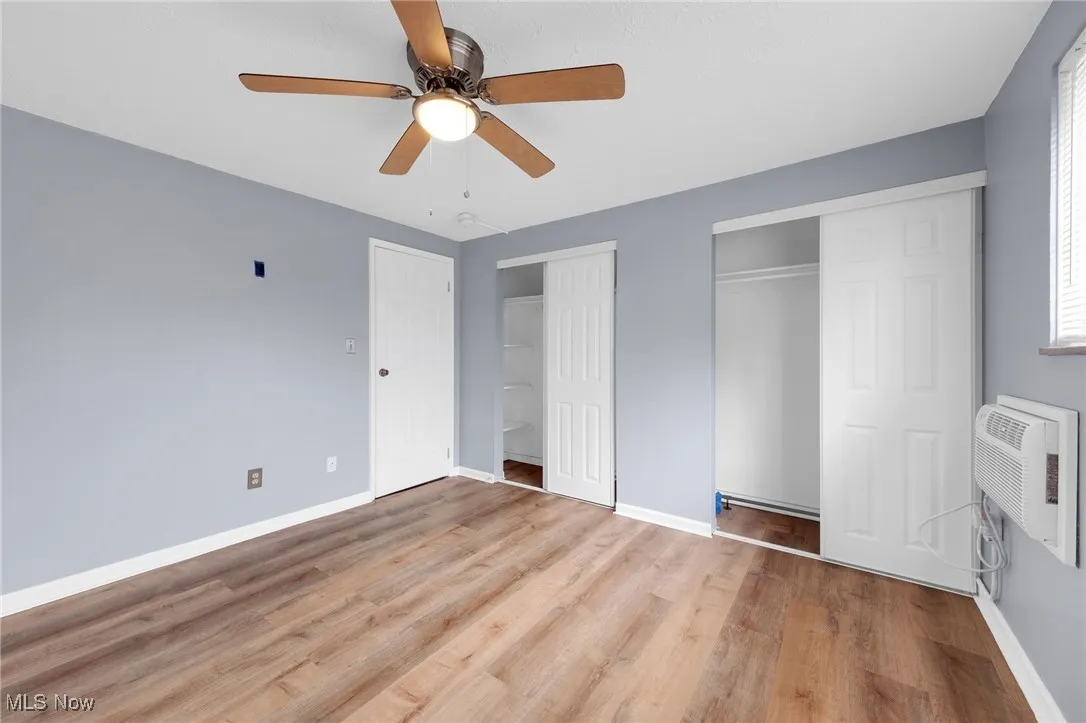 Unfurnished bedroom with two closets, light wood finished floors, a wall mounted AC, and a ceiling fan