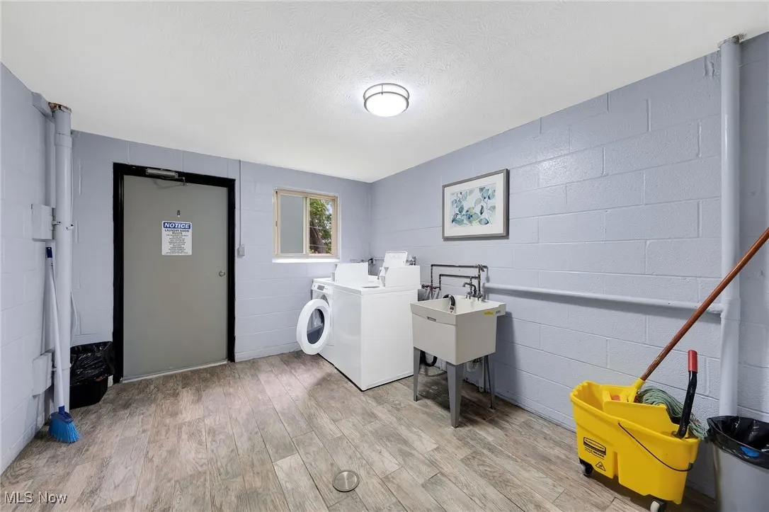 Laundry room featuring washer and dryer, light wood-type flooring, concrete block wall, and a textured ceiling