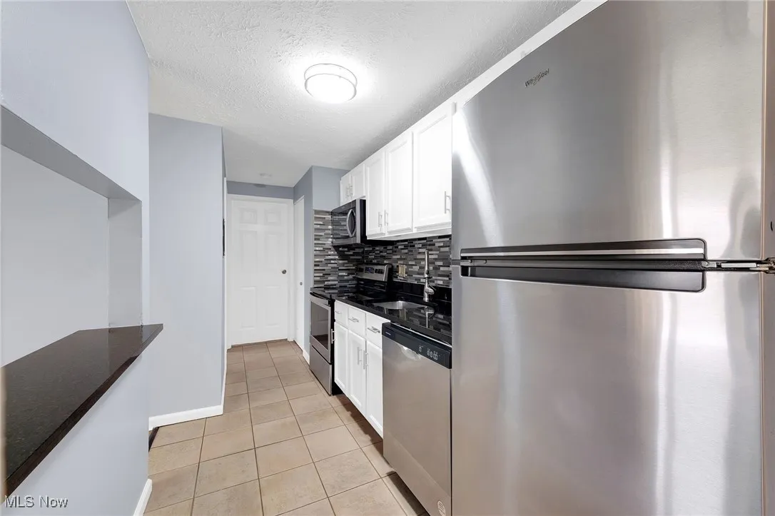 Kitchen with appliances with stainless steel finishes, white cabinets, decorative backsplash, light tile patterned flooring, and a textured ceiling