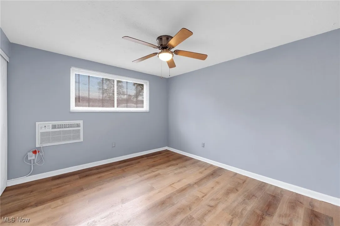 Empty room featuring a wall unit AC, a ceiling fan, and wood finished floors