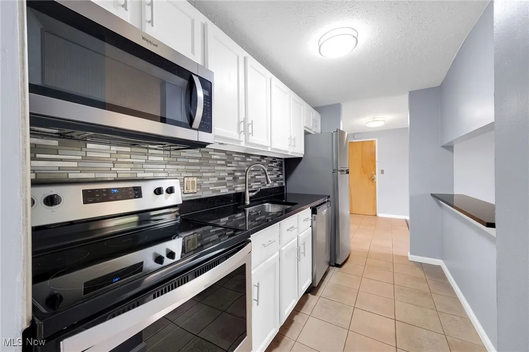 Kitchen with stainless steel appliances, white cabinetry, backsplash, light tile patterned floors, and a textured ceiling