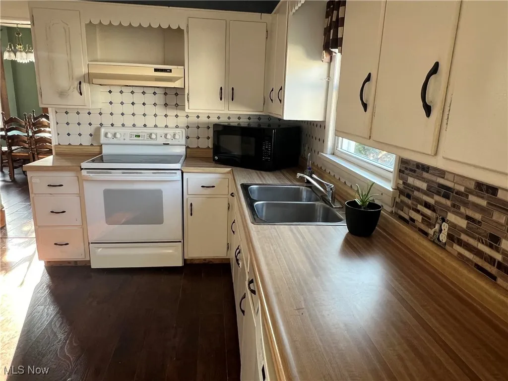 Kitchen with black microwave, white electric range, under cabinet range hood, open shelves, and light countertops