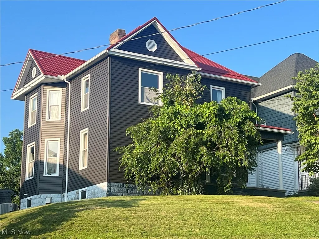 View of property exterior with a lawn, a chimney, and a metal roof