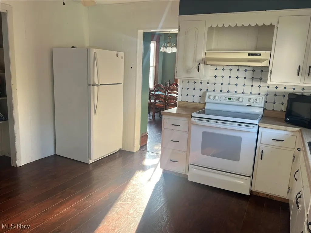 Kitchen featuring white appliances, under cabinet range hood, light countertops, and dark wood-style flooring