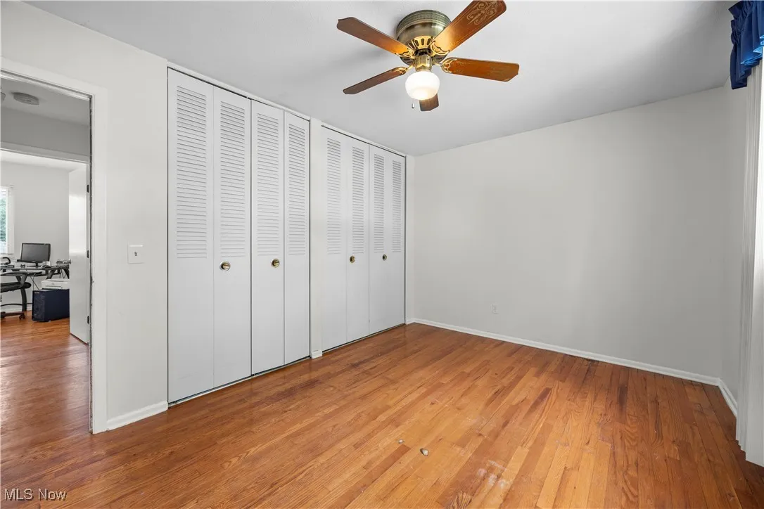 Unfurnished bedroom with a desk, wood finished floors, a ceiling fan, and multiple closets