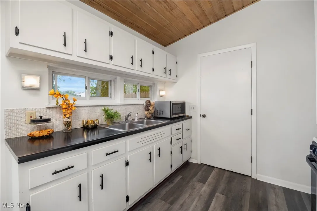 Kitchen featuring stainless steel microwave, dark countertops, backsplash, wood ceiling, and white cabinetry
