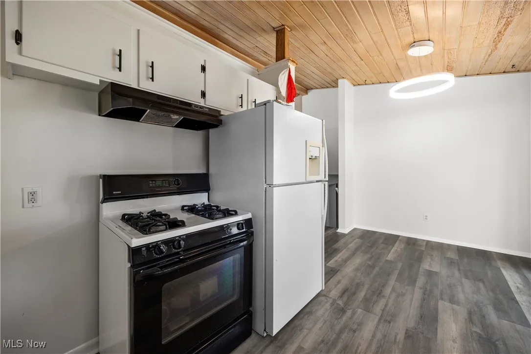 Kitchen with under cabinet range hood, gas range, wood ceiling, white cabinetry, and freestanding refrigerator