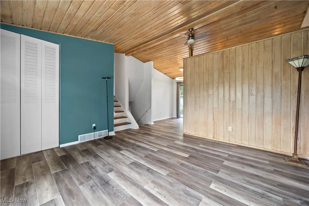 Unfurnished living room featuring vaulted ceiling, stairs, wooden ceiling, wood walls, and ceiling fan