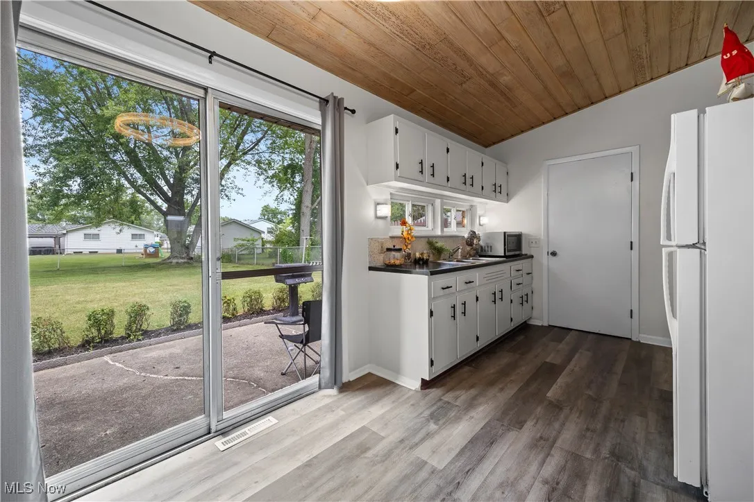 Kitchen with freestanding refrigerator, dark countertops, dark wood-type flooring, stainless steel microwave, and white cabinets