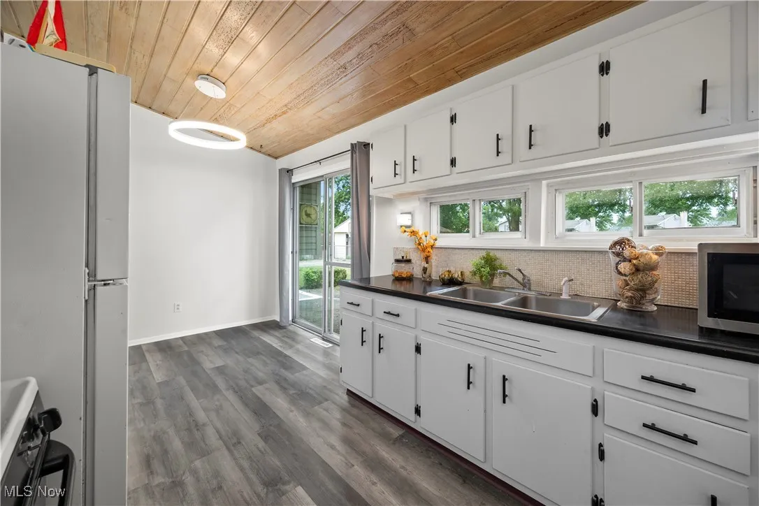 Kitchen with freestanding refrigerator, stainless steel microwave, wooden ceiling, tasteful backsplash, and dark countertops