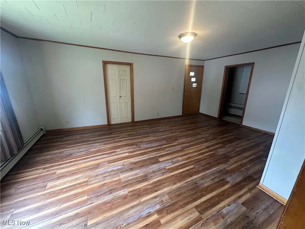 Spare room featuring wood finished floors, ornamental molding, a baseboard radiator, and radiator heating unit