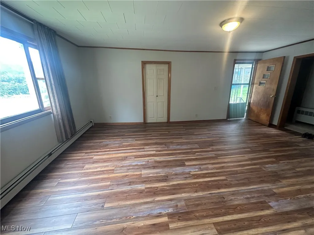 Spare room with a baseboard heating unit, wood finished floors, ornamental molding, and a baseboard radiator