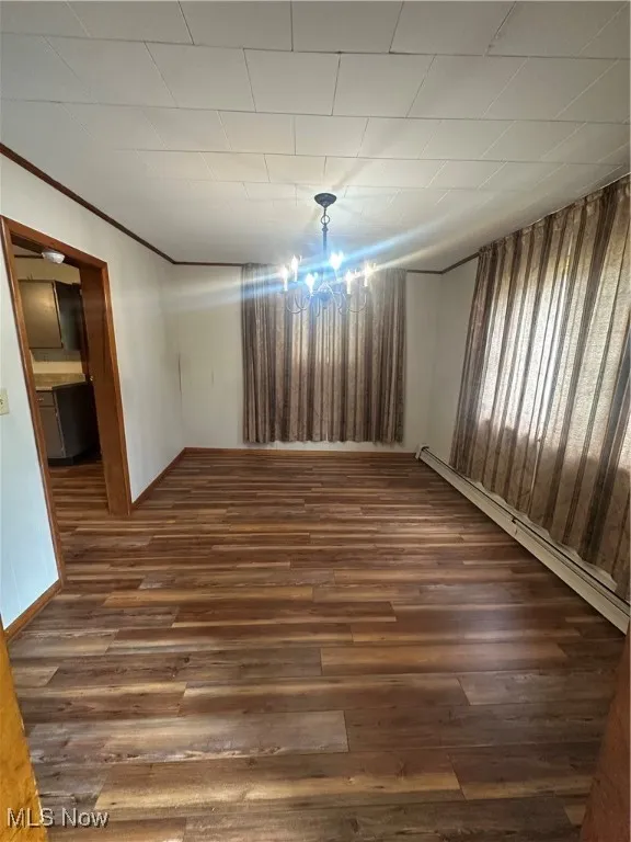 Spare room featuring dark wood-style floors, a baseboard heating unit, and crown molding