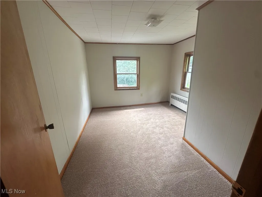 Empty room with radiator, carpet flooring, and ornamental molding