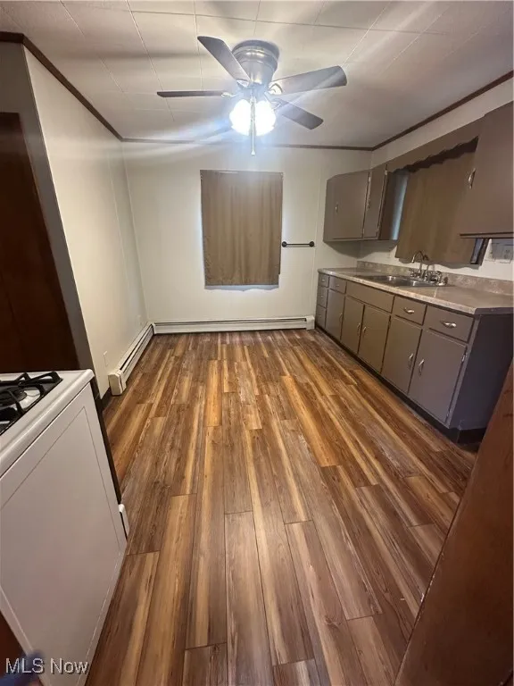 Kitchen featuring gray cabinetry, stove, a ceiling fan, dark wood finished floors, and a baseboard radiator