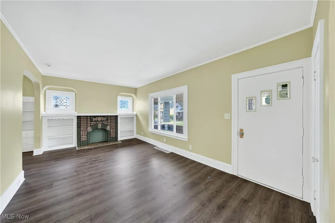 Unfurnished living room featuring dark wood-type flooring, ornamental molding, and a brick fireplace