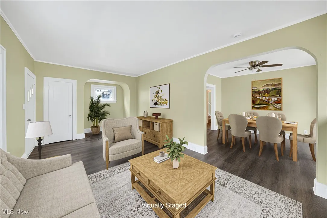 Living room with arched walkways, wood finished floors, ornamental molding, and a ceiling fan