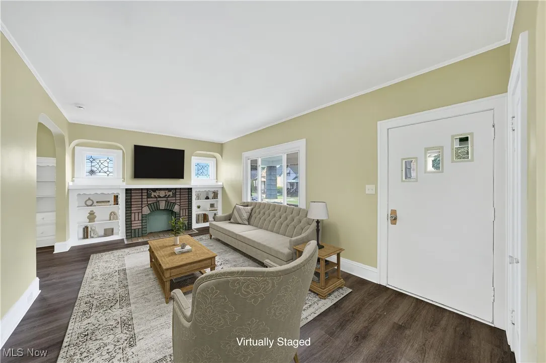 Living room featuring dark wood finished floors, ornamental molding, and a brick fireplace