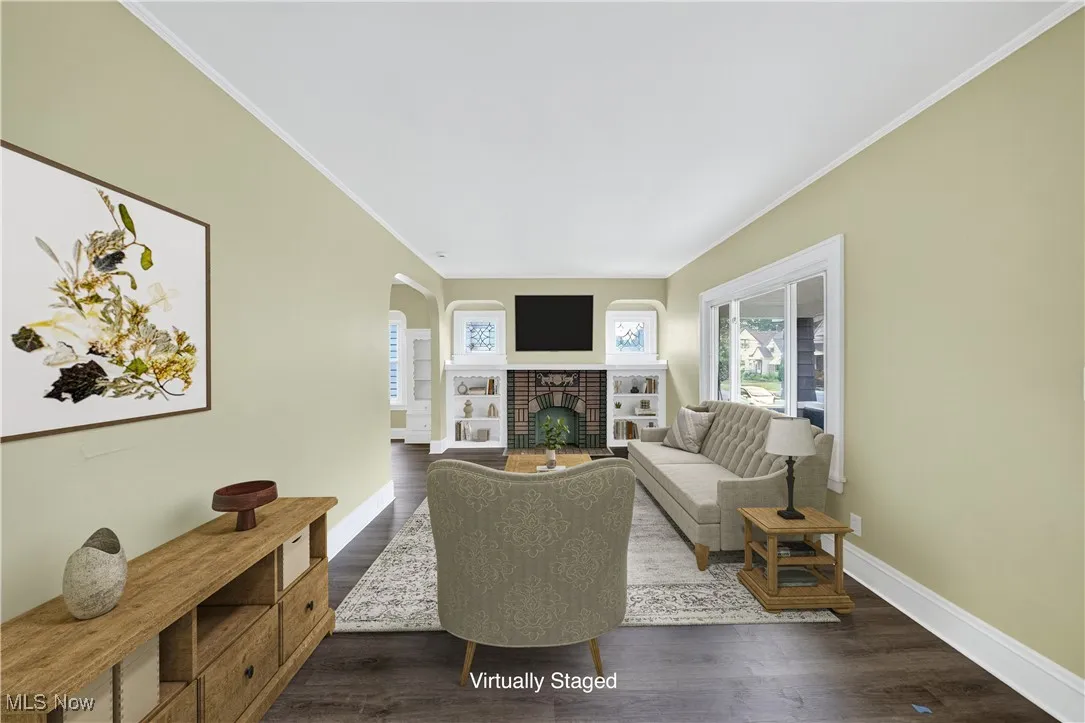 Living area featuring arched walkways, dark wood-type flooring, crown molding, and a brick fireplace