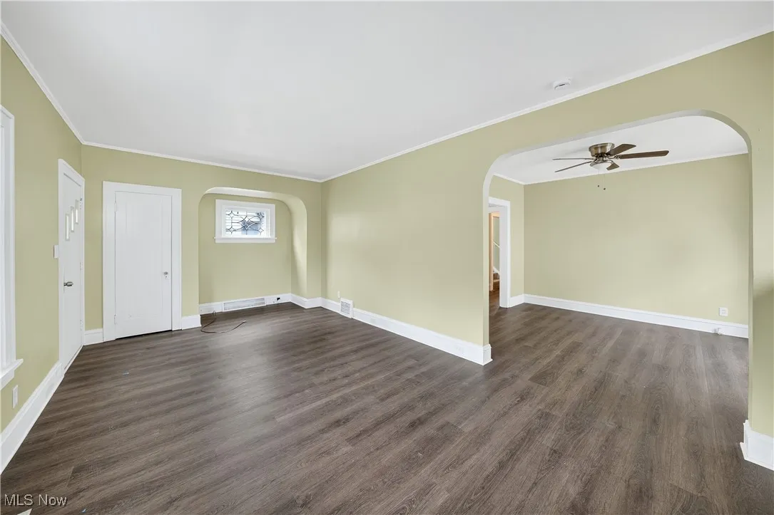 Empty room with arched walkways, ceiling fan, dark wood-style flooring, crown molding, and a smoke detector