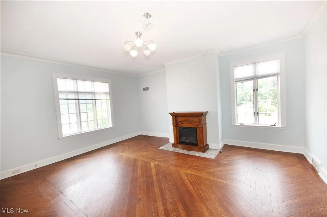 Unfurnished living room with crown molding, a chandelier, and a fireplace with flush hearth
