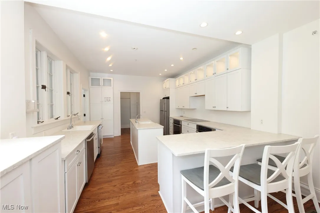 Kitchen featuring appliances with stainless steel finishes, wood finished floors, a kitchen island, white cabinetry, and recessed lighting