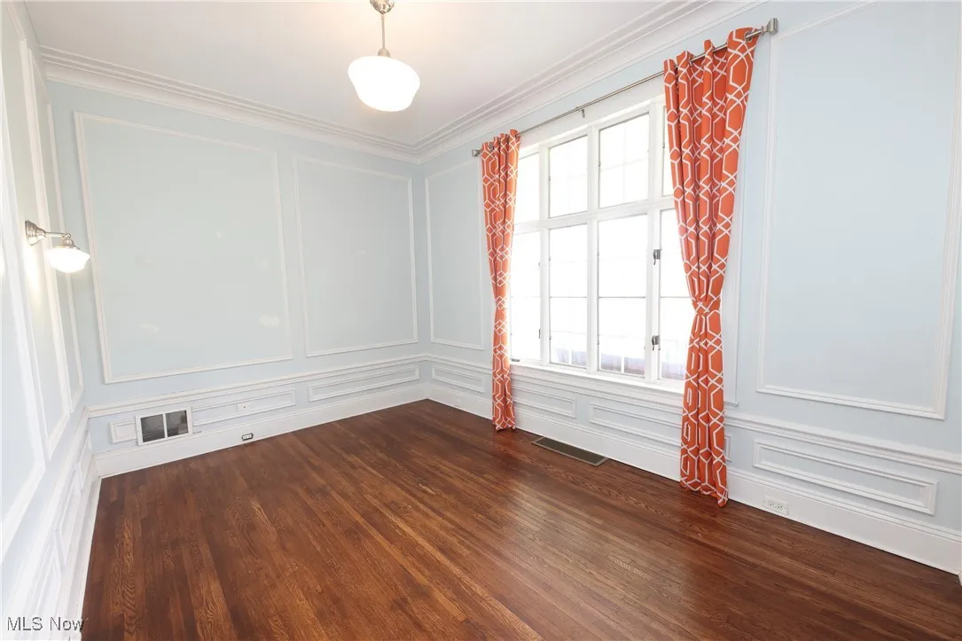 Empty room with a decorative wall, dark wood-style flooring, and ornamental molding