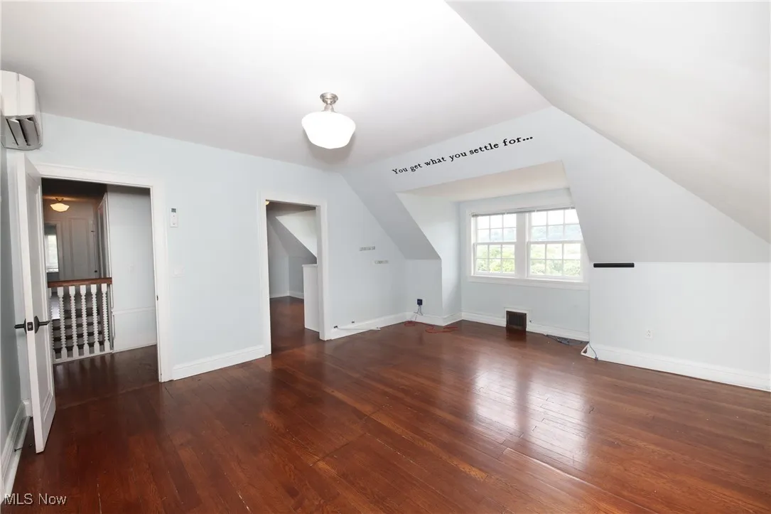 Additional living space with a wall mounted AC, wood-type flooring, and lofted ceiling