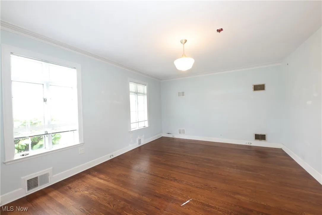 Unfurnished room featuring healthy amount of natural light, crown molding, and dark wood-type flooring