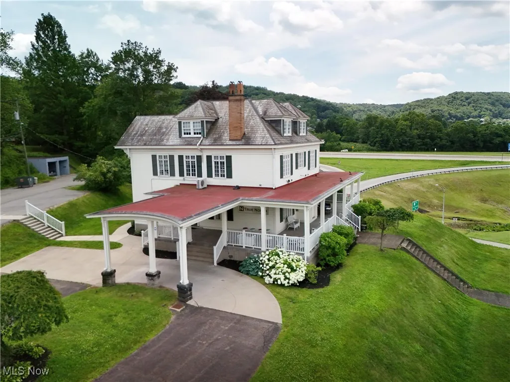 View of front of house featuring a porch, driveway, a chimney, a front lawn, and a view of trees