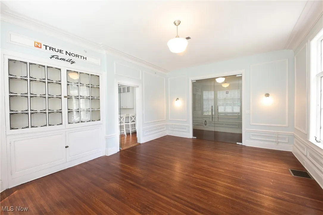 Empty room with a decorative wall, wood finished floors, and crown molding
