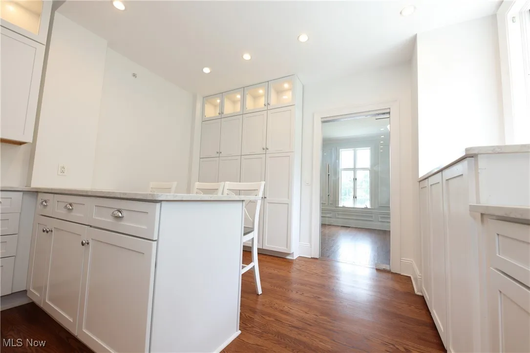 Kitchen featuring dark wood-style flooring, a peninsula, glass insert cabinets, recessed lighting, and white cabinetry
