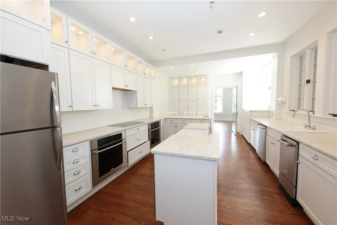 Kitchen featuring stainless steel appliances, a center island with sink, white cabinetry, light stone counters, and recessed lighting