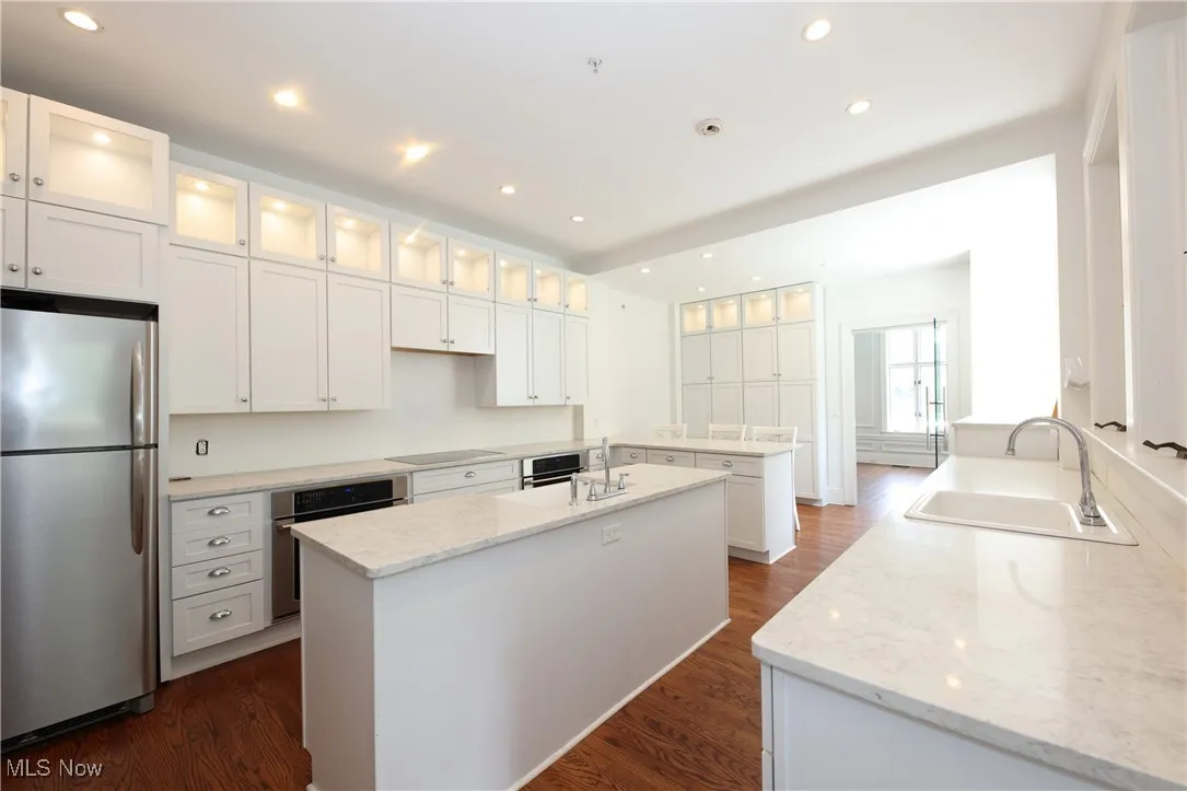 Kitchen with stainless steel appliances, a center island with sink, dark wood-style flooring, light stone countertops, and recessed lighting