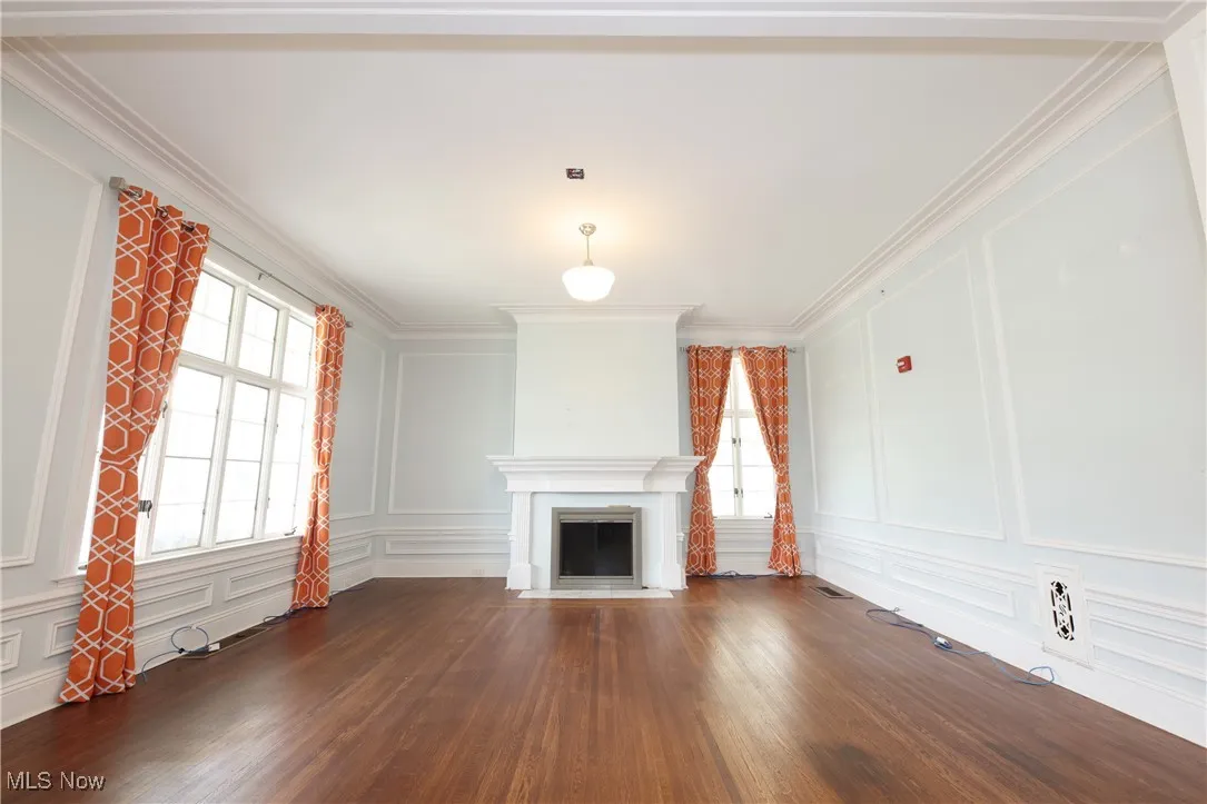 Unfurnished living room with a decorative wall, dark wood finished floors, crown molding, and a fireplace with flush hearth