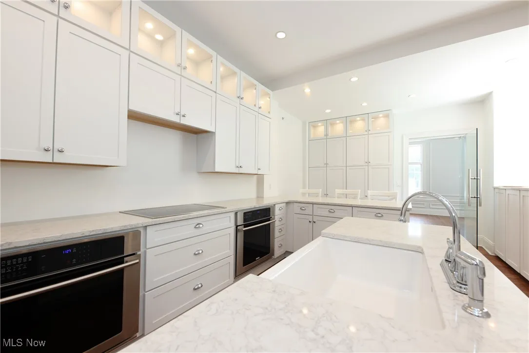 Kitchen with stainless steel oven, black electric stovetop, white cabinetry, and recessed lighting