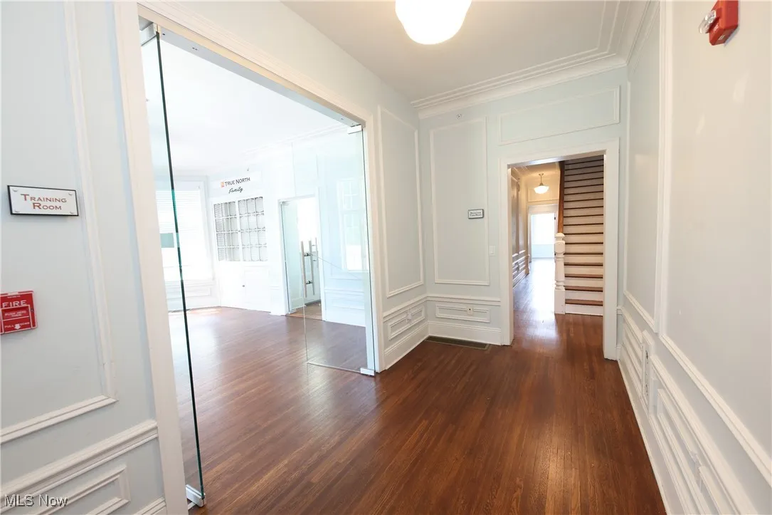 Hallway with a decorative wall, dark wood-style floors, and crown molding