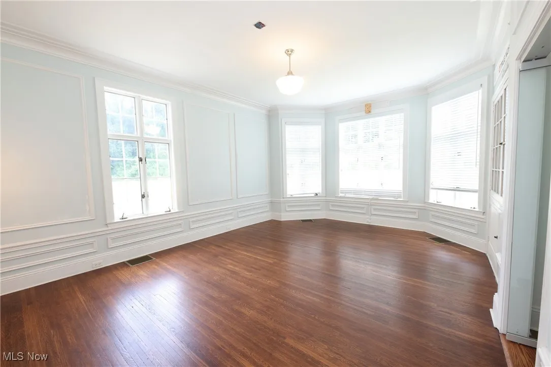 Empty room featuring a decorative wall, ornamental molding, and dark wood-style floors