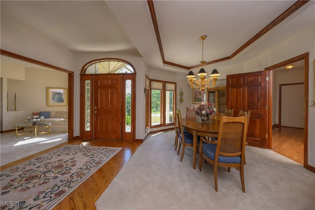 Dining area with a chandelier, wood finished floors, a tray ceiling, and crown molding