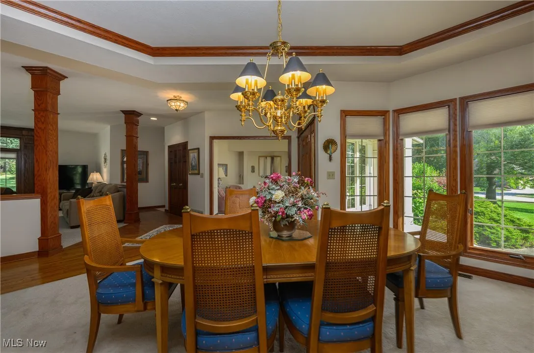 Dining space featuring ornate columns, ornamental molding, a chandelier, and light colored carpet