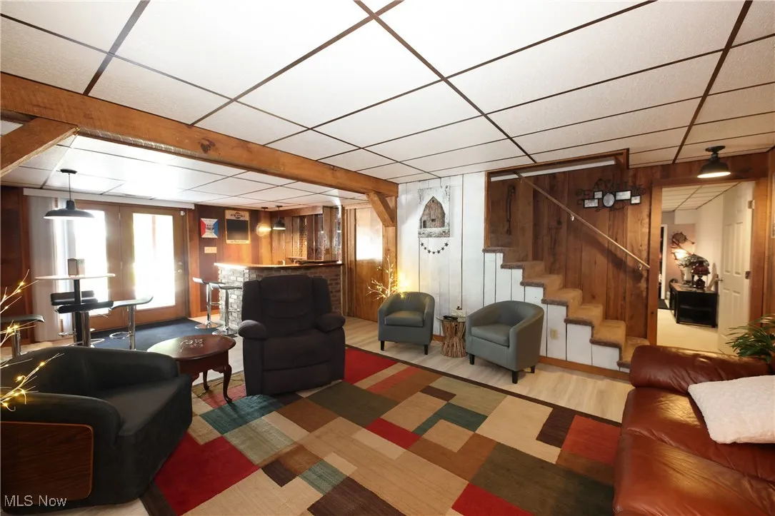 Living area featuring wooden walls, stairway, a paneled ceiling, and wood finished floors