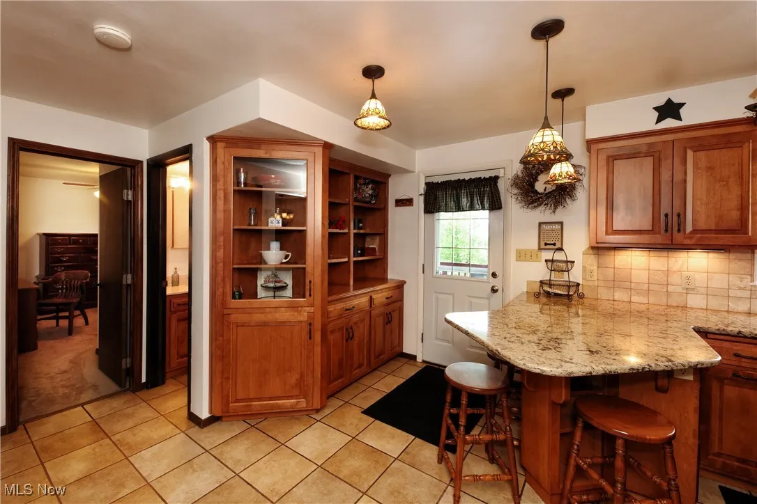Kitchen featuring a peninsula, a kitchen breakfast bar, decorative backsplash, brown cabinets, and pendant lighting