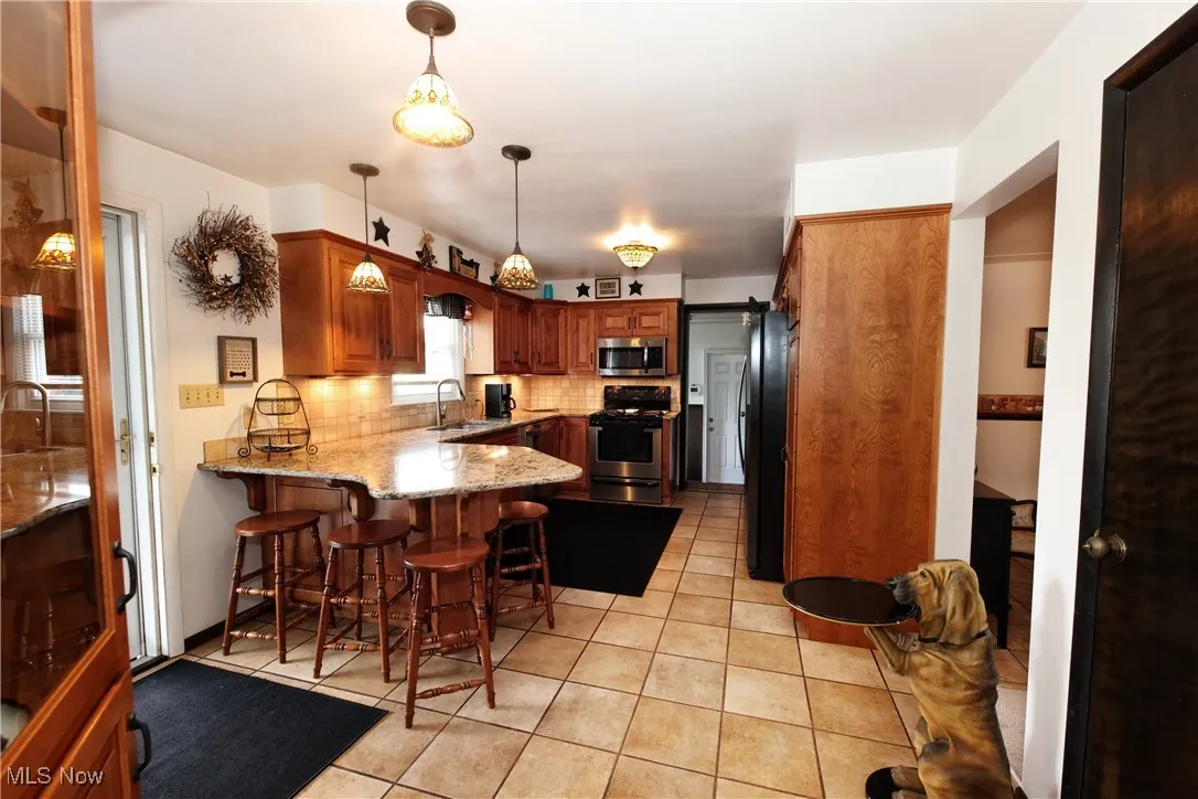 Kitchen featuring stainless steel appliances, a peninsula, decorative backsplash, light stone countertops, and light tile patterned floors