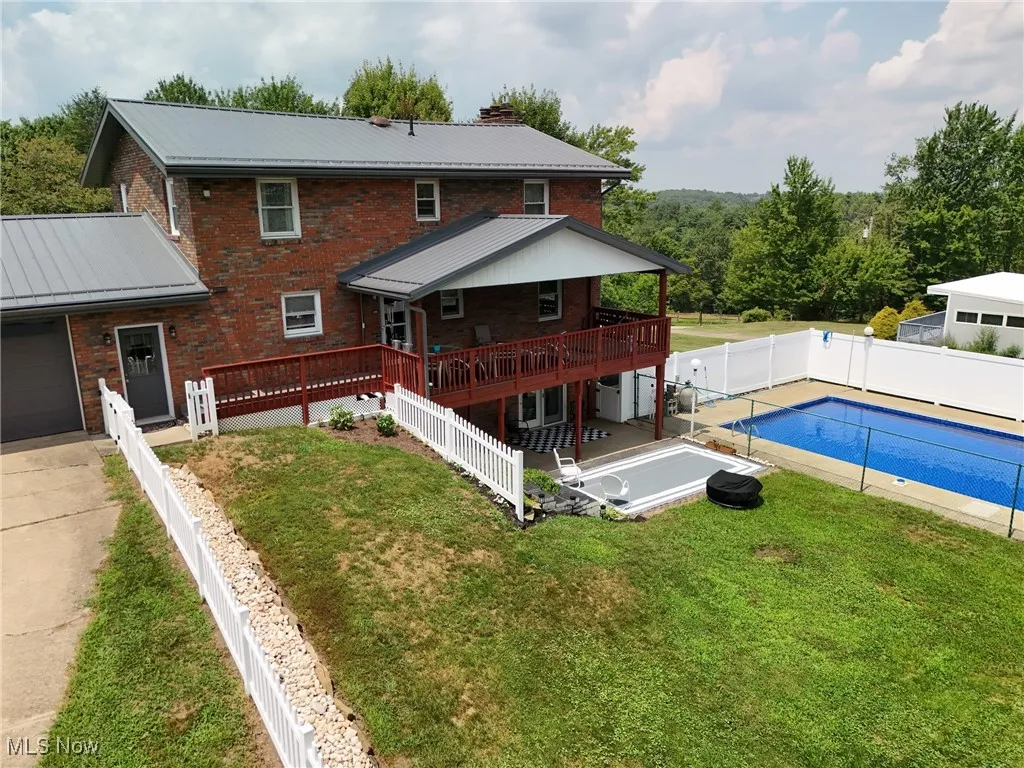 Rear view of property with brick siding, a wooden deck, a metal roof, and a fenced backyard