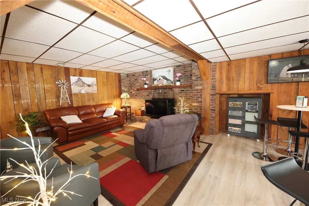 Living room featuring wooden walls, wood finished floors, a drop ceiling, and a brick fireplace